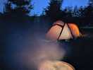 Nighttime. firepit in foreground, orange tent lit from inside