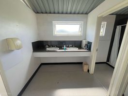 Sinks with extra toilet rolls in the box to the right and cleaning supplies.