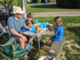 Family meal at camping les deux plages: two kids and a dad in a hat sitting at a camping table