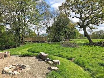 Fire pit beside river, with bridge and old oak beyond